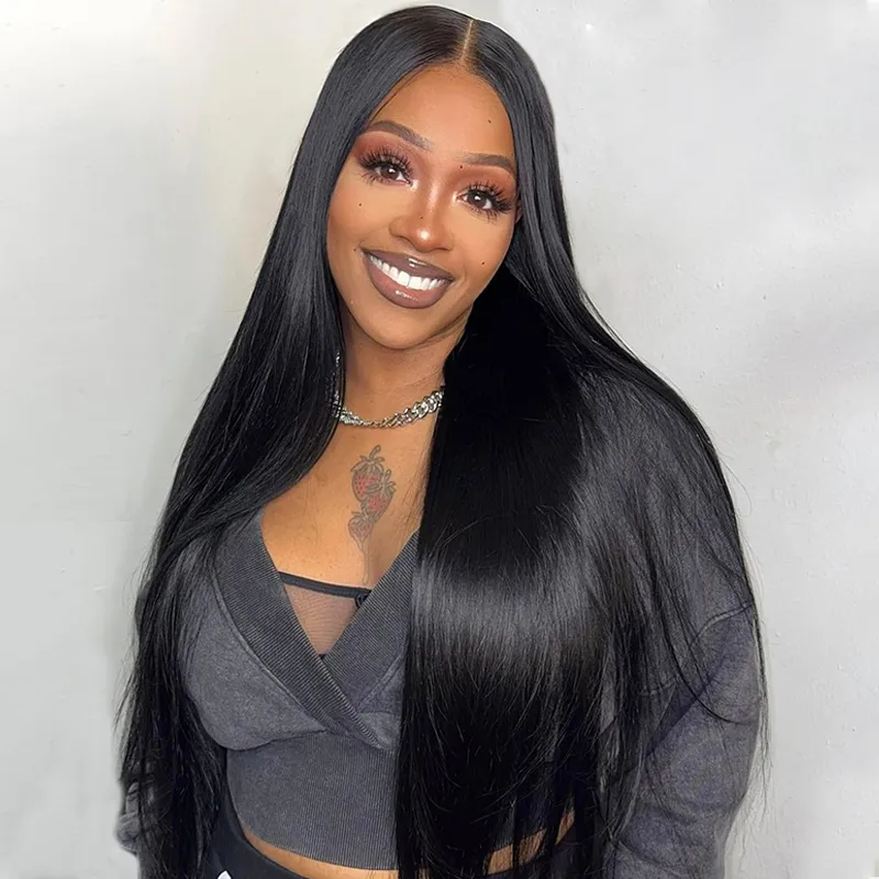 Smiling woman with long, straight black hair wearing a gray cropped top and a silver chain necklace; tattoo of a rose on her chest is visible.